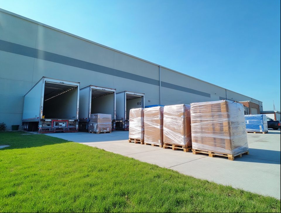 Wrapped pallets being sorted beside several open trailer doors under a bright blue sky