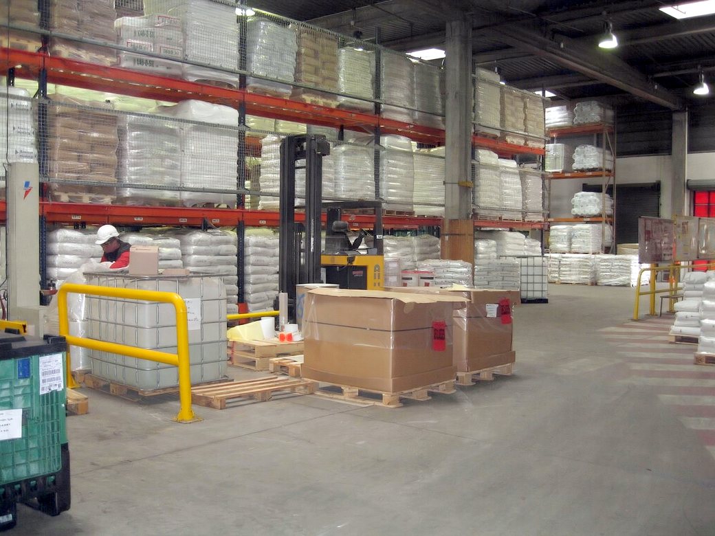Inside the Gratton Warehouse facility in Omaha: tall orange pallet racking stocked with bagged goods, a reach truck, and boxed pallets staged on the floor